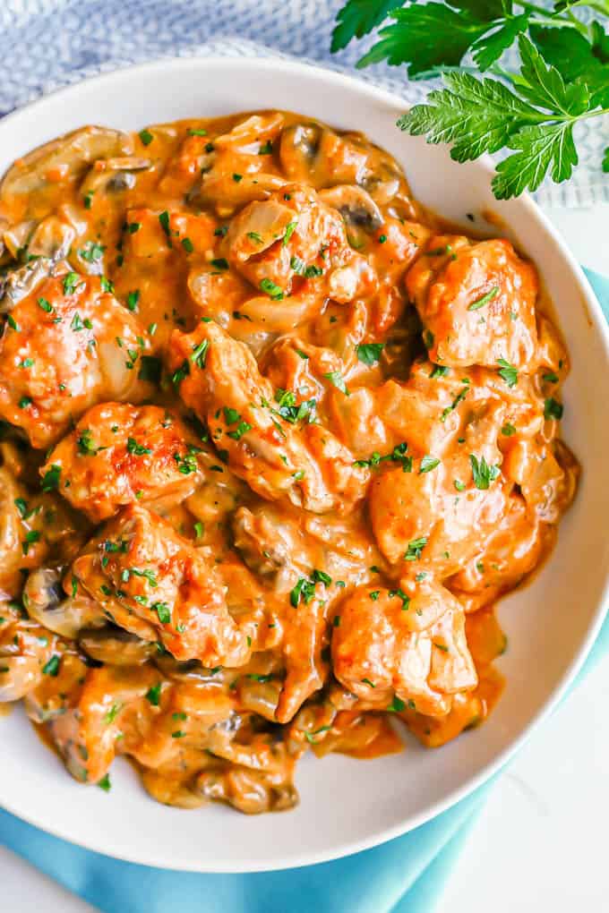 A low white bowl with a quick and easy chicken paprikash in a creamy sauce with fresh parsley on top