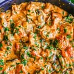 Close up of creamy chicken paprikash in a large skillet with mushrooms and onions mixed in and fresh parsley sprinkled on top with a text overlay on the photo.
