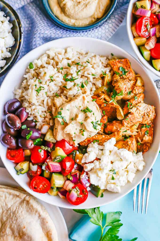Chicken shawarma served with brown rice, veggies, olives, feta cheese and hummus in a low serving bowl