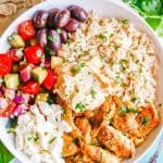A low white bowl with brown rice, chicken shawarma, fresh veggies, olives, feta and hummus with a text overlay on the photo