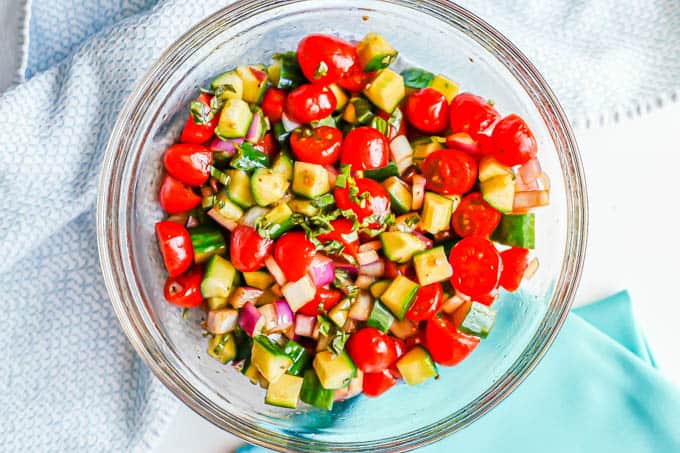 A cucumber tomato red onion salad with basil and a balsamic dressing in a clear bowl