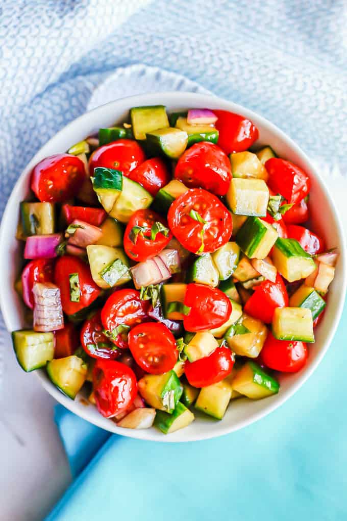 A marinated cucumber tomato red onion salad served in a small white bowl with fresh basil