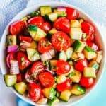 A marinated cucumber tomato red onion salad served in a small white bowl with fresh basil and a text overlay on the photo