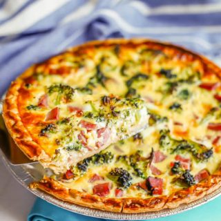 A slice of quiche with ham and broccoli being lifted from a baked pie pan