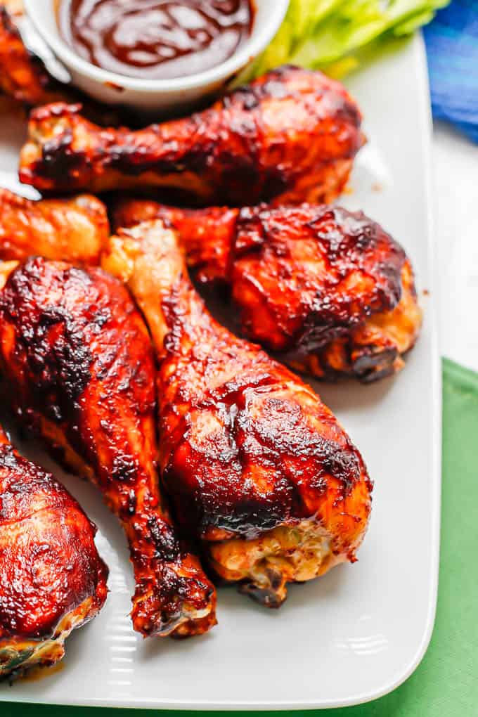 Close up of BBQ chicken legs served on a white platter with a small bowl of BBQ sauce