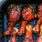 Close up of BBQ basted chicken legs in an Air Fryer after cooking with a text overlay on the photo