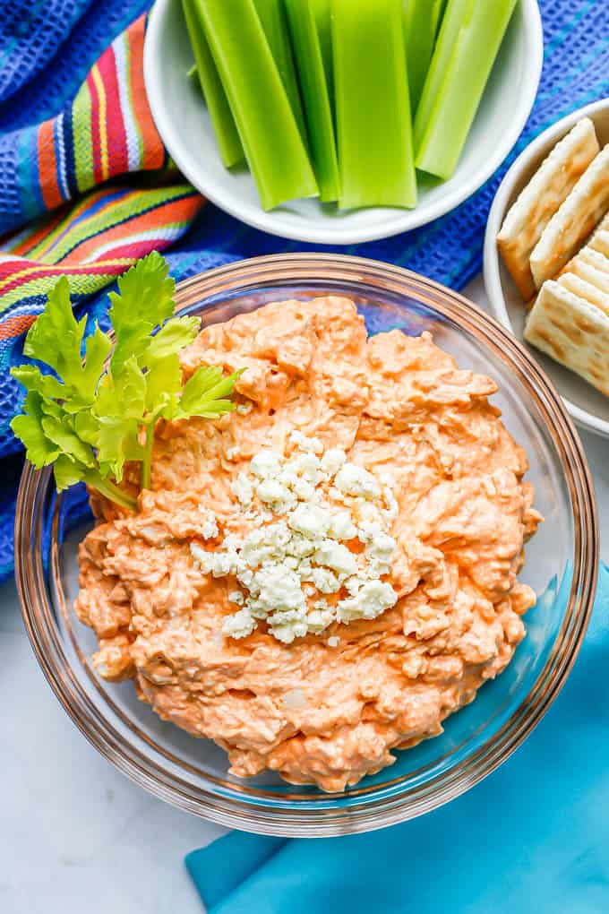 Buffalo chicken dip served in a glass bowl with blue cheese crumbles on top and a garnish of celery leaves
