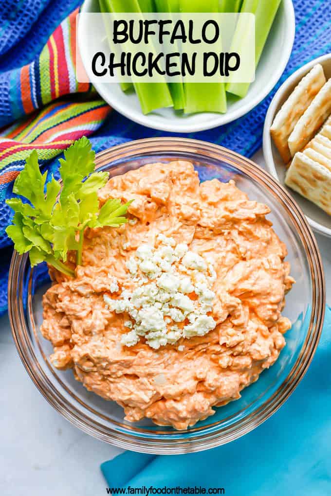 Buffalo chicken dip served in a glass bowl with blue cheese crumbles on top and a garnish of celery leaves with a text box on the photo