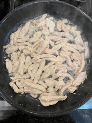 Strips of chicken cooking in a large skillet