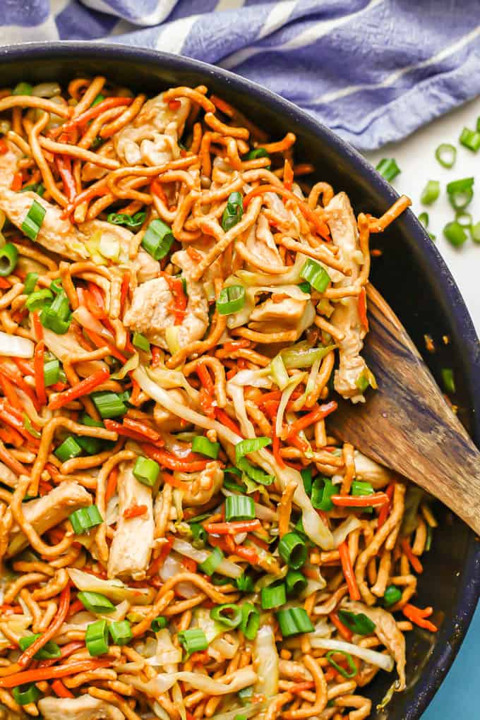 A wooden spoon resting in a large skillet of prepared chicken chow mein