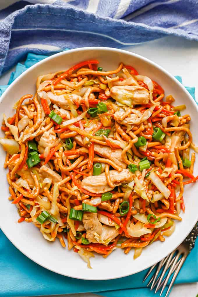 Homemade chicken chow mein served in a low white bowl with sliced green onions on top and forks to the side