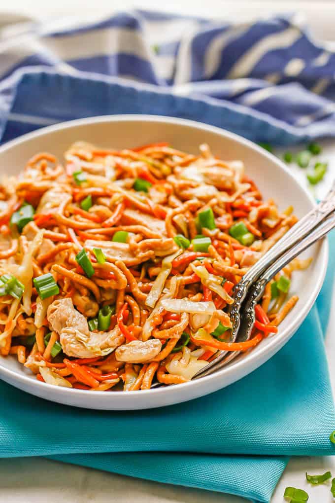 Two forks resting in a low white bowl with a serving of chicken chow mein