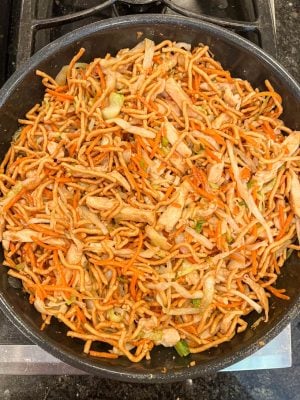 Chicken chow mein being made in a skillet on the stove