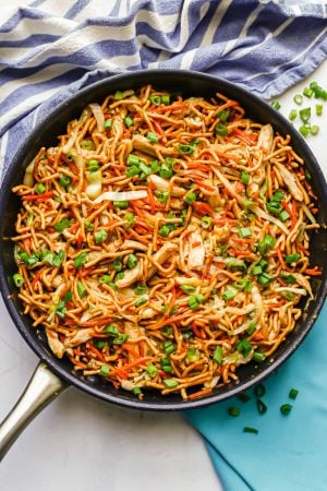 Chicken chow mein in a large dark skillet with green onions sprinkled on top and to the side of the pan