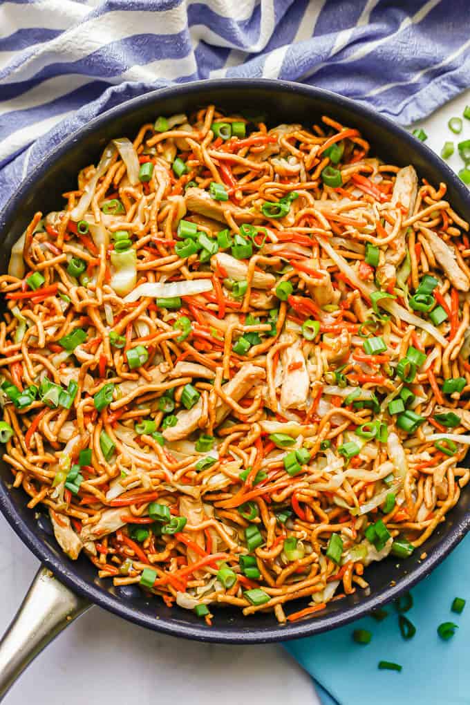 Homemade chicken chow mein in a large dark skillet with green onions sprinkled on top and to the side of the pan