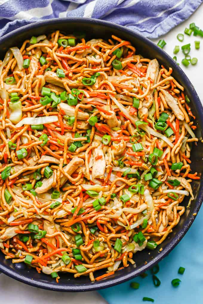 Easy chicken chow mein in a large dark skillet with green onions sprinkled on top and to the side of the pan