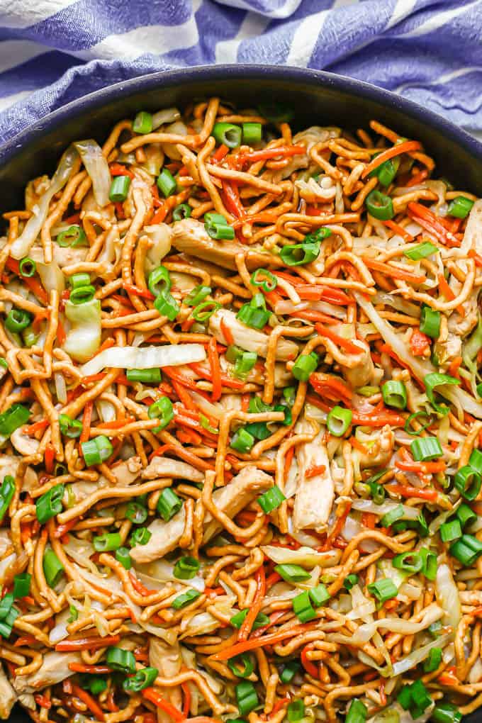 Close up of chicken chow mein in a large dark skillet with green onions sprinkled on top and to the side of the pan