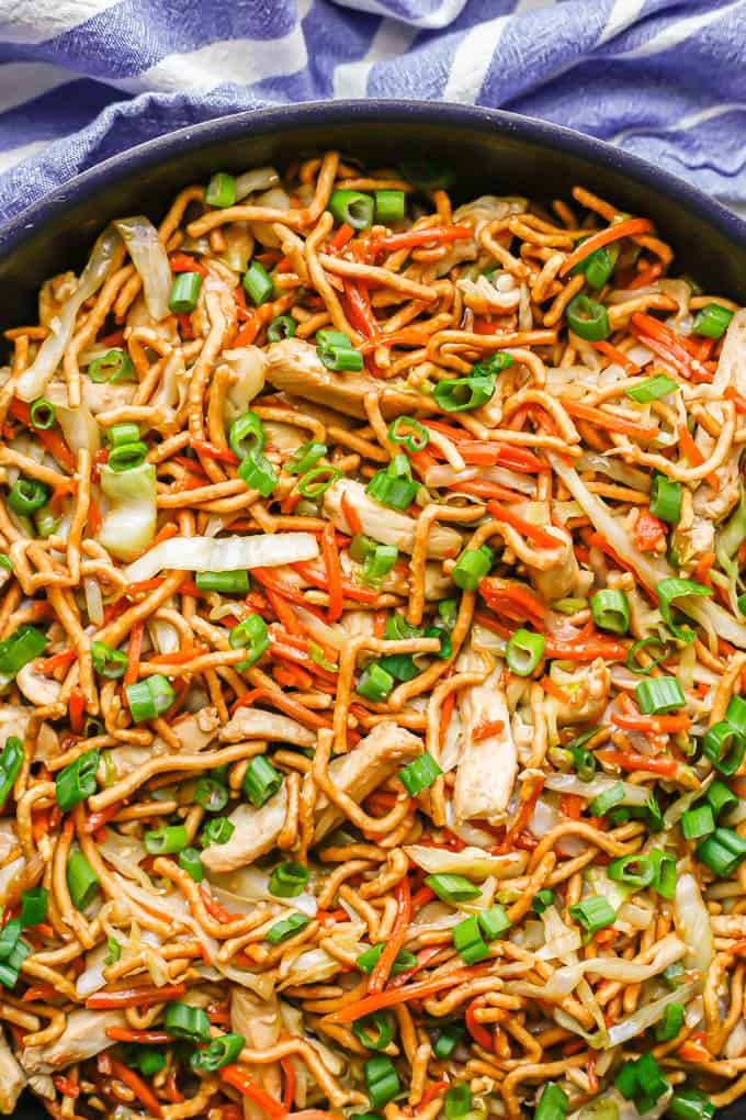 Close up of chicken chow mein in a large dark skillet with green onions sprinkled on top and to the side of the pan