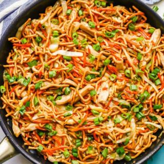 Overhead of chicken chow mein in a large dark skillet with green onions sprinkled on top and to the side of the pan
