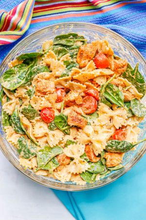 Chicken and pasta with spinach, tomatoes and a hummus sauce in a large glass bowl