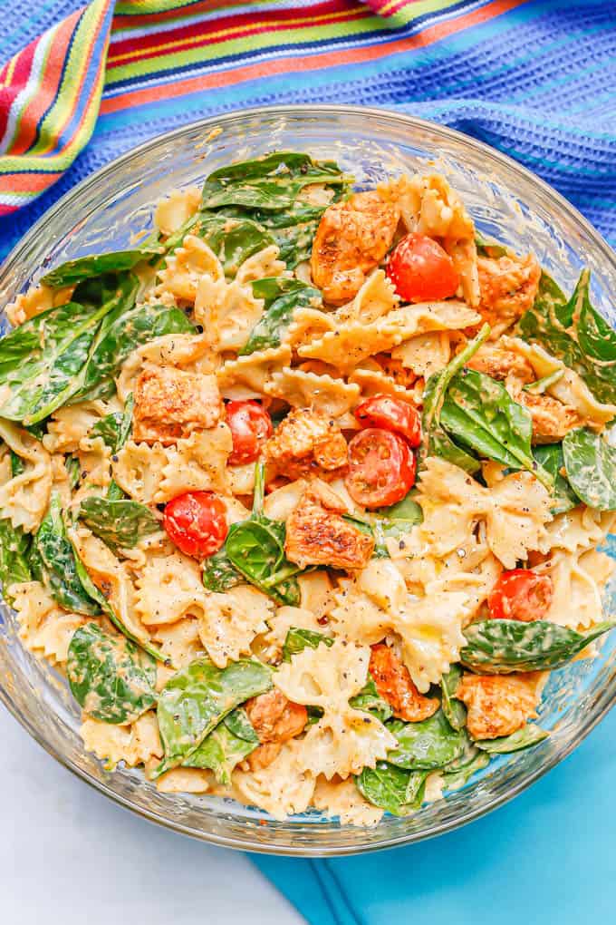 A large glass bowl with chicken and pasta with spinach, tomatoes and a hummus sauce