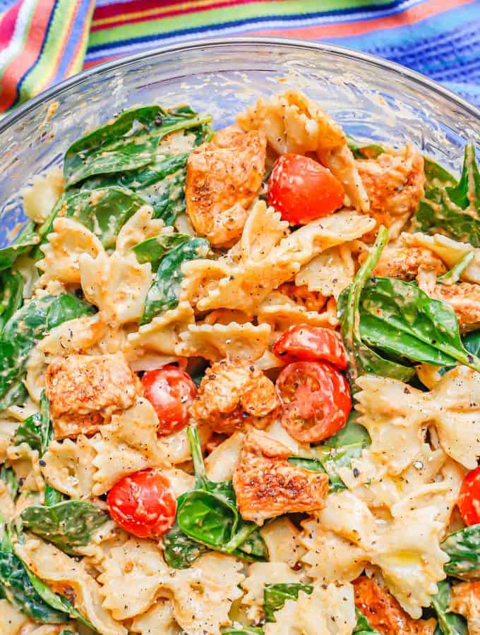 Close up of a chicken pasta with vegetables and a hummus sauce in a large glass bowl