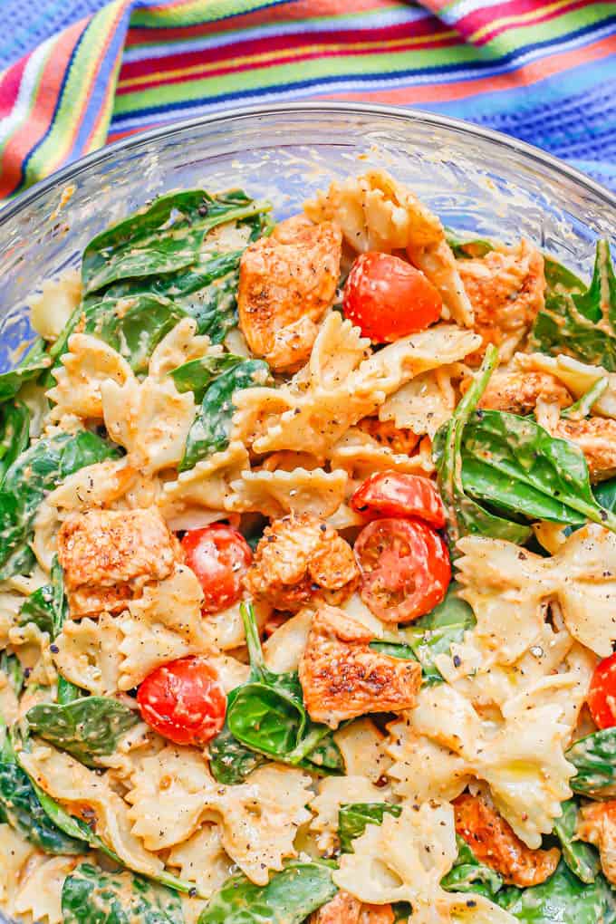 Close up of a chicken pasta with vegetables and a hummus sauce in a large glass bowl