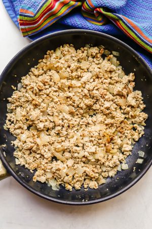 Cooked, crumbled ground chicken with onions in a large dark skillet