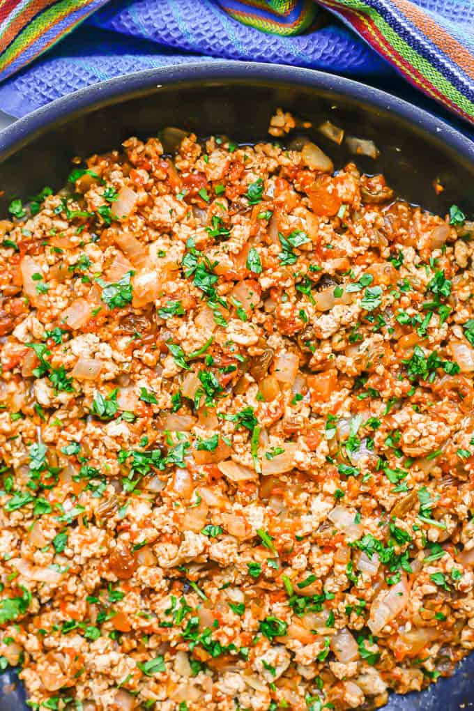 A large dark skillet with a ground chicken mixture with onions and salsa mixed in, topped with chopped cilantro