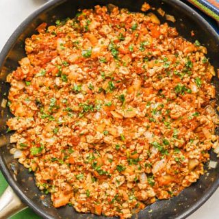 Ground chicken mixture with salsa and onions topped with cilantro in a large dark skillet