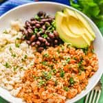 Low white bowl with chicken picadillo topped with cilantro served with rice, black beans and avocado with a text overlay on the photo