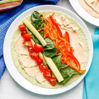 A tortilla spread with hummus and topped with colorful fresh veggies