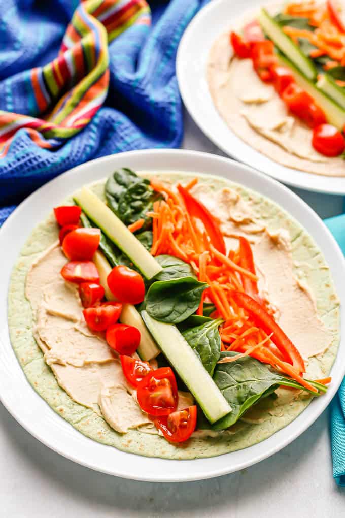 Two white plates with hummus and veggie wraps laid out