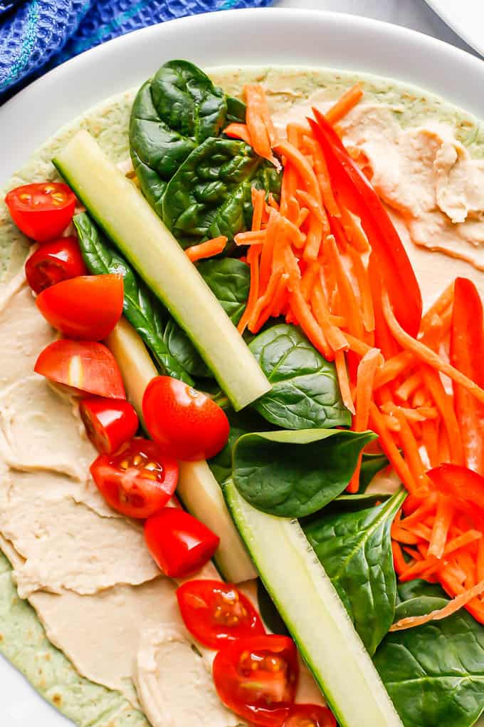 Close up of a tortilla with hummus and veggies on a white plate