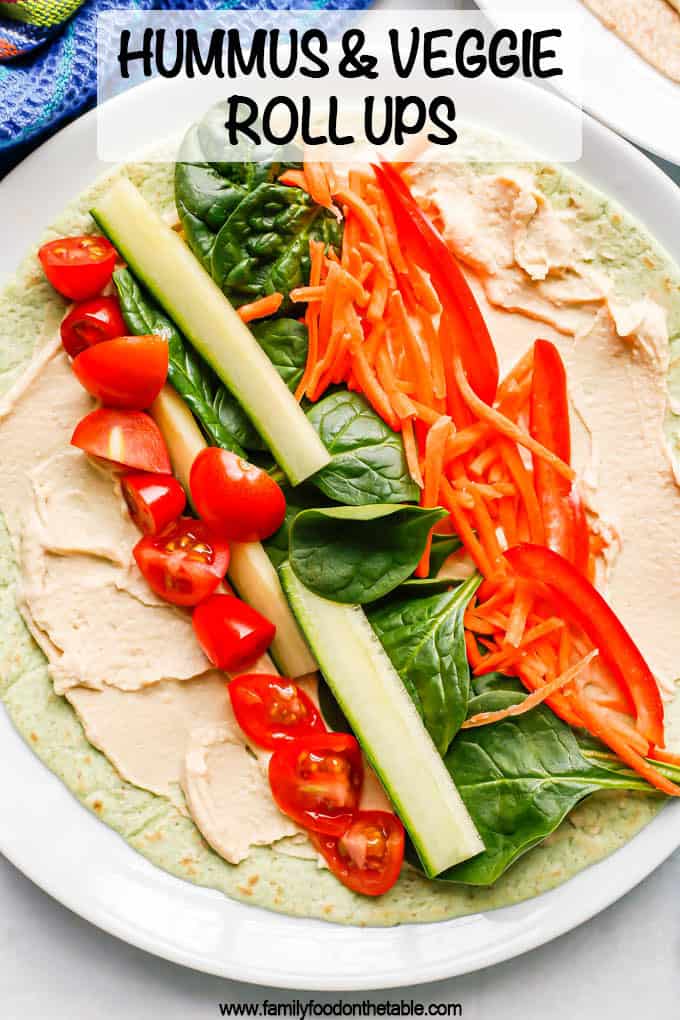 A white plate with a spinach tortilla layered with hummus, tomato, cucumber, spinach, carrots and peppers with a text box on the photo