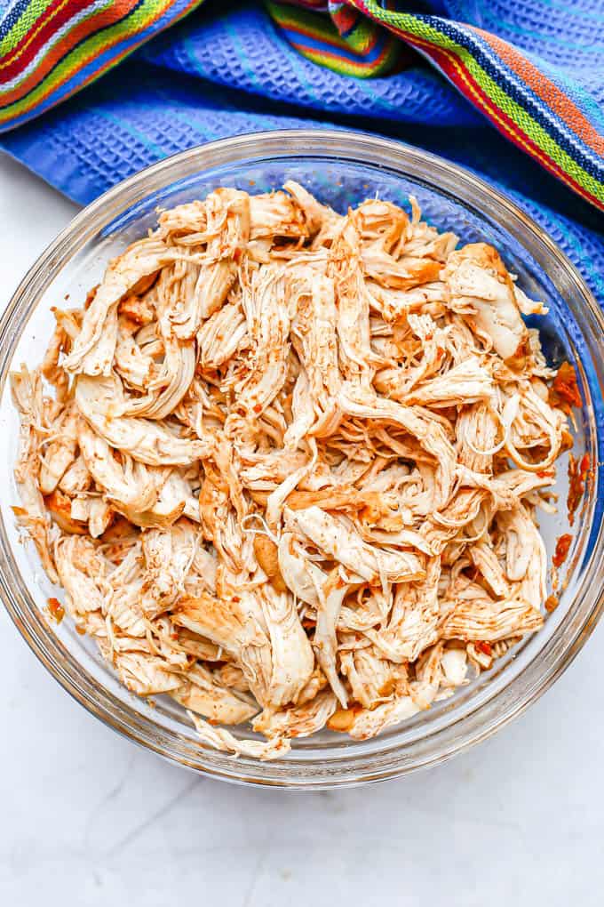 Cooked, shredded chicken in a large glass bowl with a striped blue towel in the background