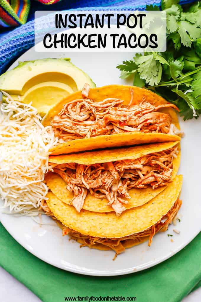 Shredded chicken tacos served on a plate with cheese, avocado and cilantro and a text overlay on the photo
