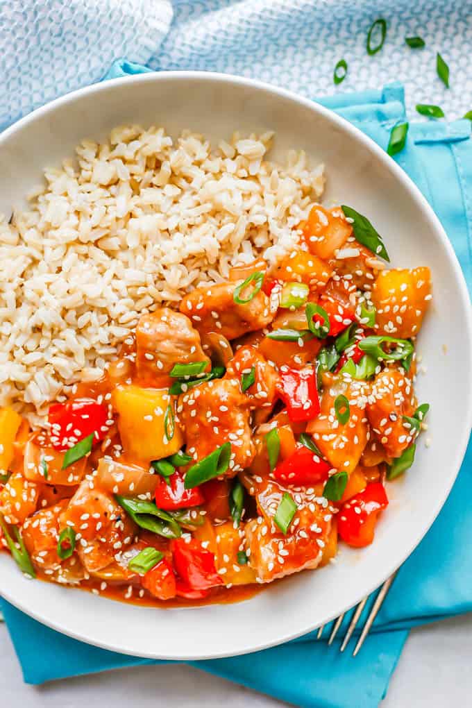 Sweet and sour pork topped with green onions and sesame seeds and served with rice in a low white bowl