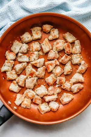 Seared and browned cubed pieces of pork in a large copper skillet