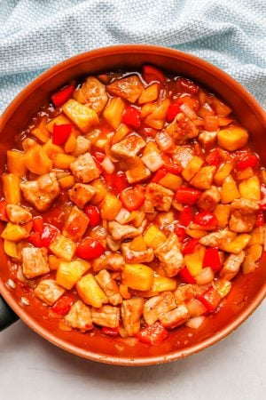 Cooked cubed pieces of pork with pineapple and bell peppers in a sauce in a copper skillet