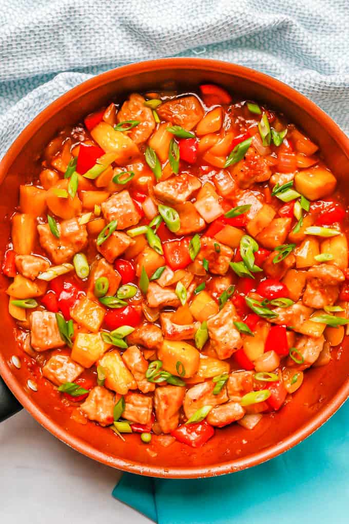 Pork chunks cooked with bell peppers, pineapple and sweet and sour sauce in a large copper skillet