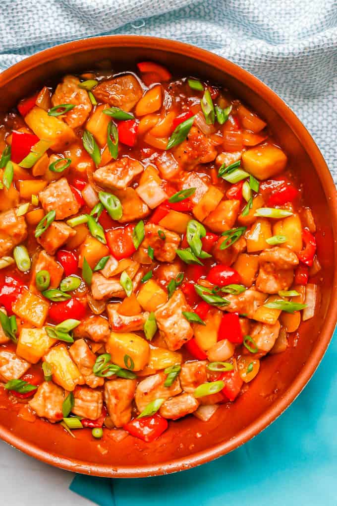 A large copper skillet with sweet and sour pork topped with green onions