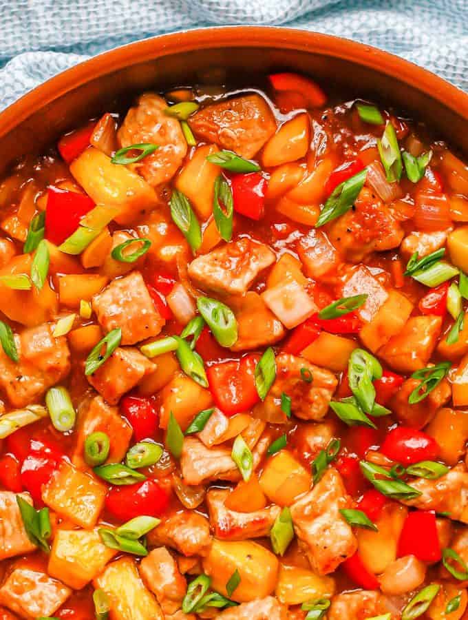 Sweet and sour pork with peppers and pineapple in a large copper skillet with sliced green onions on top