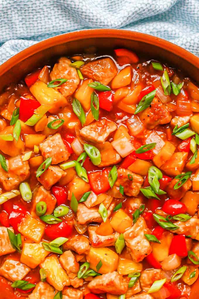 Sweet and sour pork with peppers and pineapple in a large copper skillet with sliced green onions on top