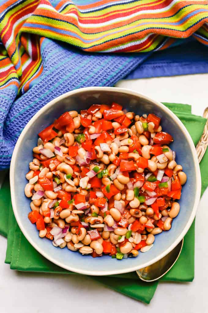 A colorful black eyed pea salad with fresh veggies in a blue bowl set on green napkins