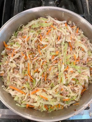 Ground turkey, cabbage and carrots being cooked in a large skillet on the stove
