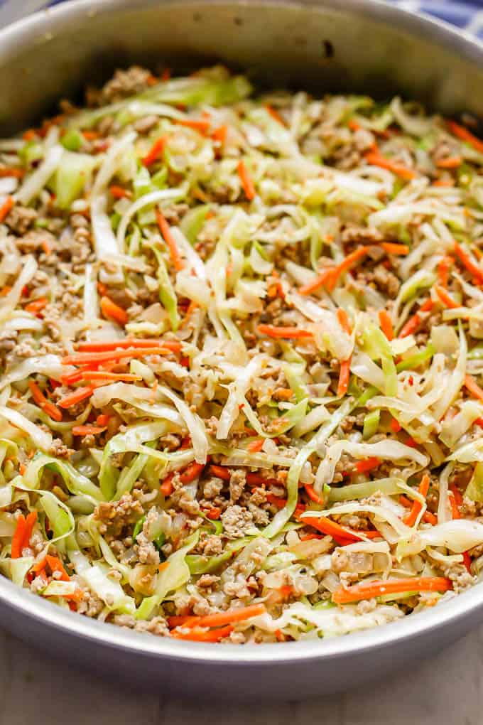 Close up of a large deep skillet with a mixture of ground turkey, shredded cabbage and shredded carrots