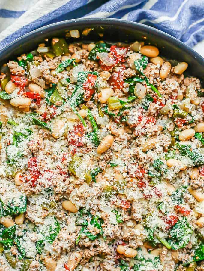 A skillet full of ground turkey, white beans, tomatoes and spinach with Parmesan cheese on top