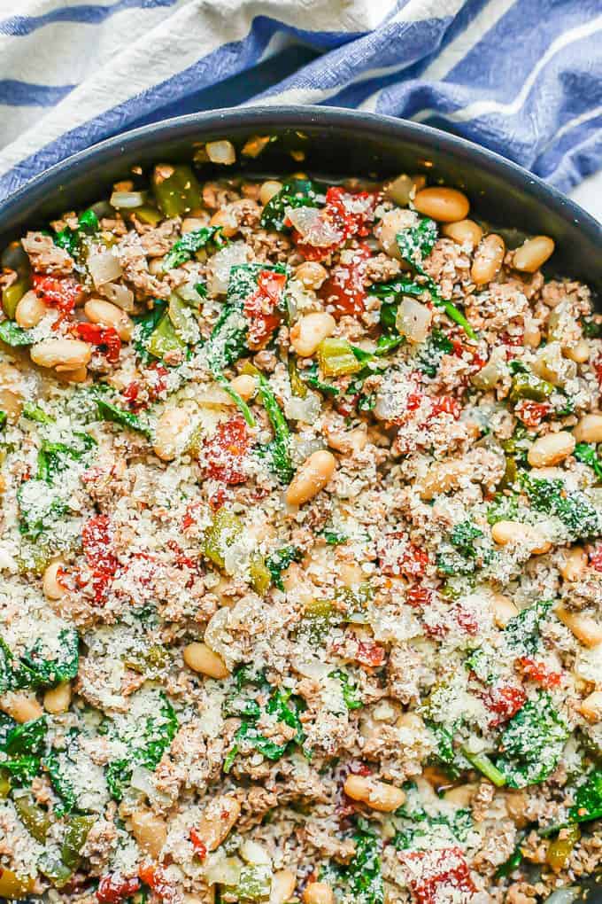 A skillet full of ground turkey, white beans, tomatoes and spinach with Parmesan cheese on top