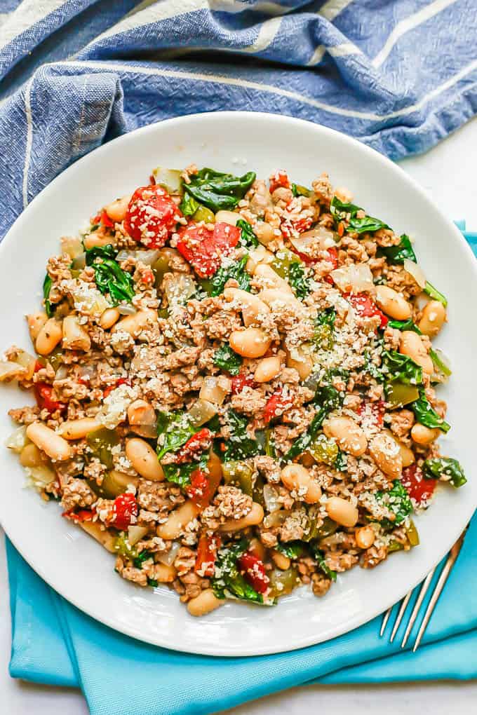 A white plate with a ground turkey mixture with white beans, tomatoes and spinach with Parmesan cheese on top
